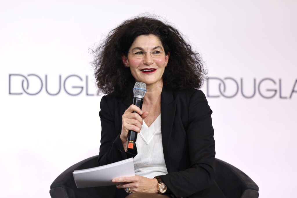 Tina Müller vor Douglas-Werbetafel spricht über ein Mikrofon