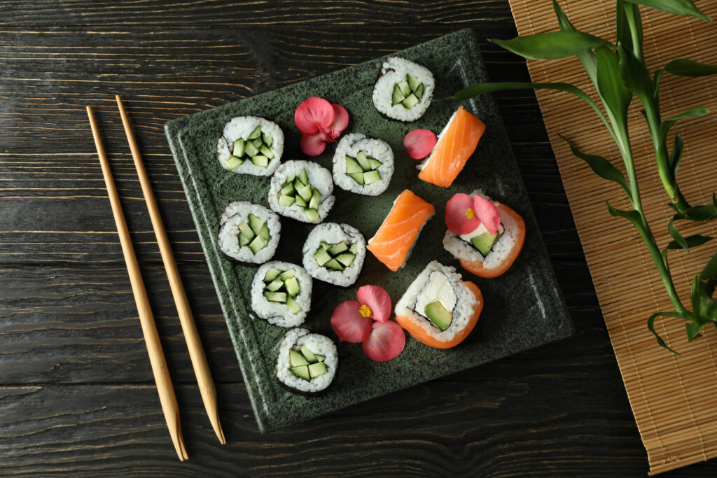 Verschiedene Sushi-Kreationen sind neben Stäbchen auf schwarzer Platte plaziert