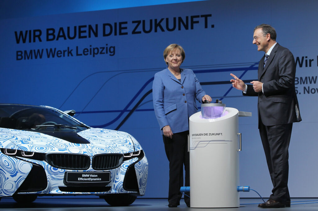 Angela Merkl steht gemeinsam mit Norbert Reithofer an einem Rednerpult. Neben ihr ein neuer BMW Vision EfficientDynamics und daher das Logo Wir bauen die Zukunft BMW Werk Leipzig
