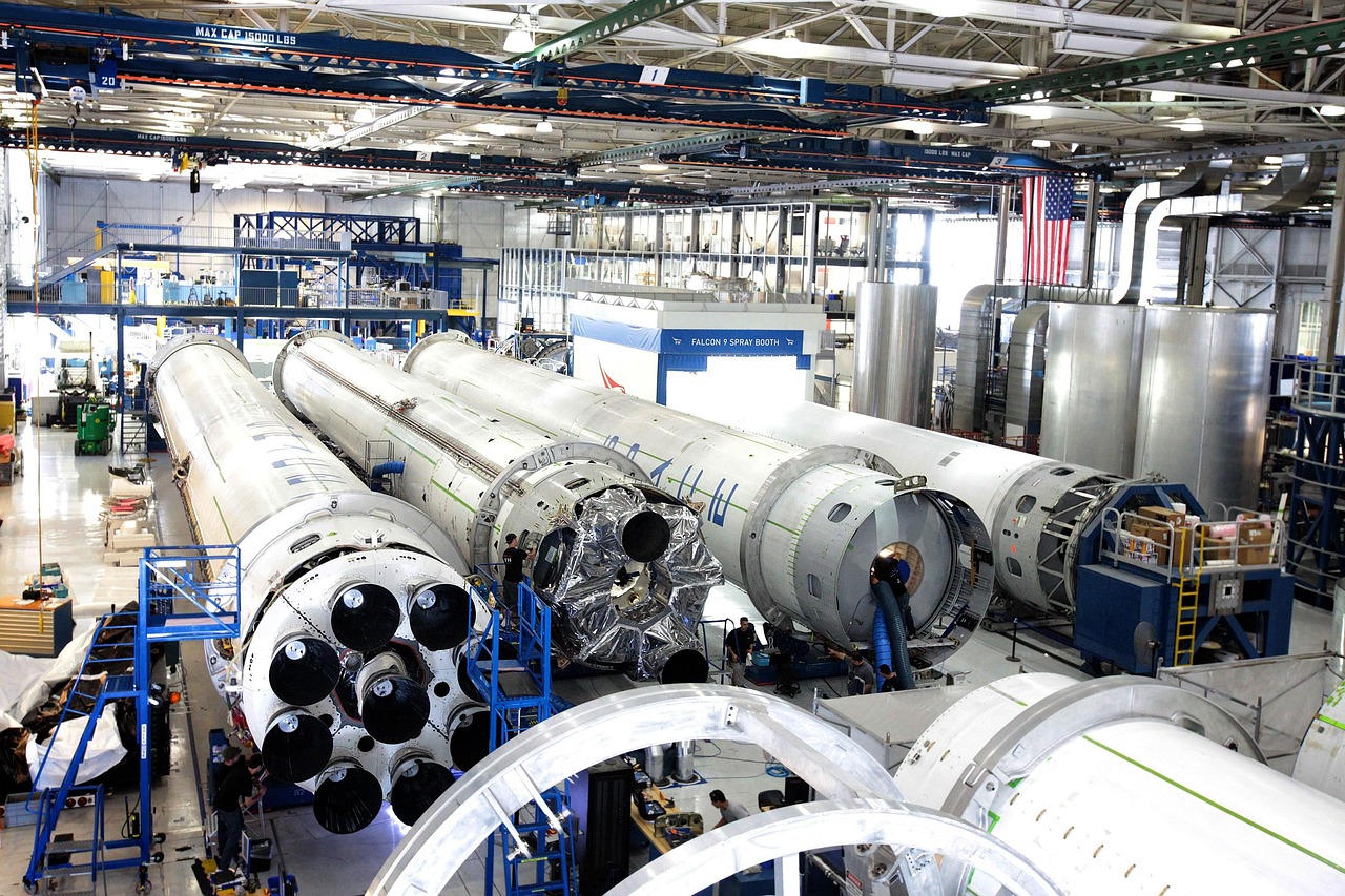 Ein Montagewerk für Elektroautos neben einem Raketenstartturm symbolisiert die mögliche Fusion der Unternehmen von Elon Musk – Foto: SpaceX-Imagery / Pixabay